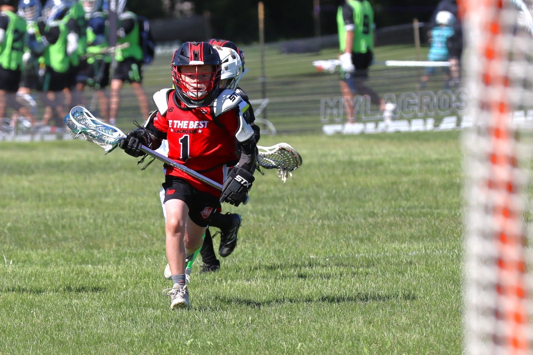 A young Be The Best boys lacrosse player carrying the ball during tournament play.